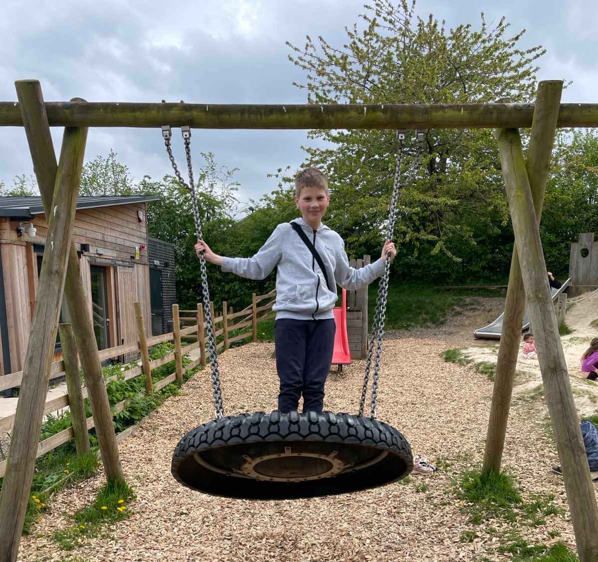 A young person standing on a tyre swing at an outdoor playground during a Mentoring Plus activity day