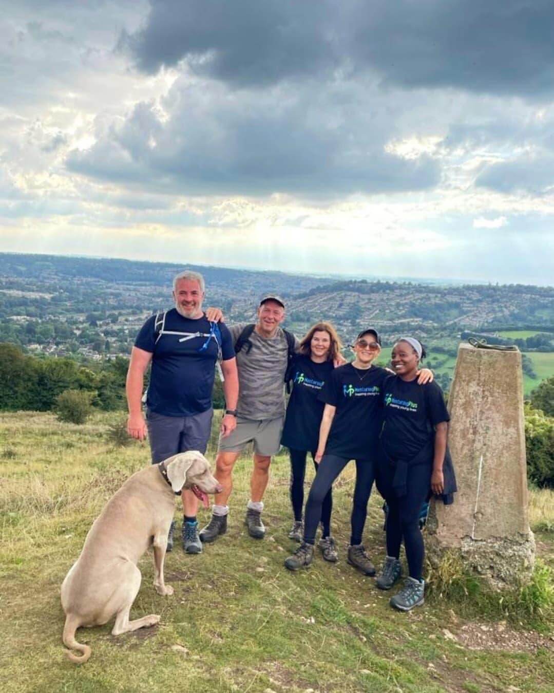 Mentoring Plus supporters and a dog standing at a hilltop trig point during a fundraising walk