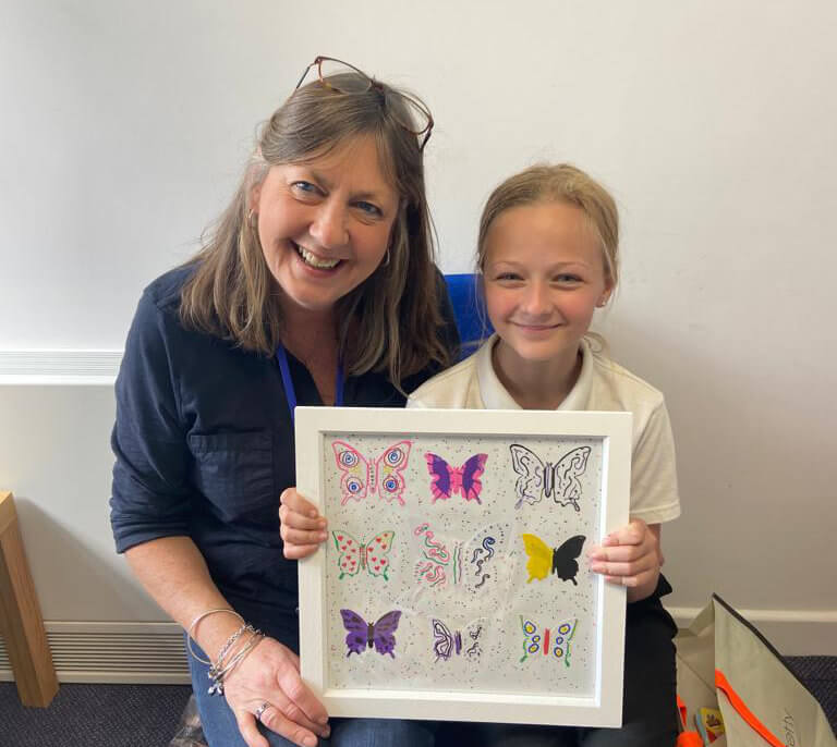 A mentor and young person smiling and holding a framed piece of butterfly artwork they made together