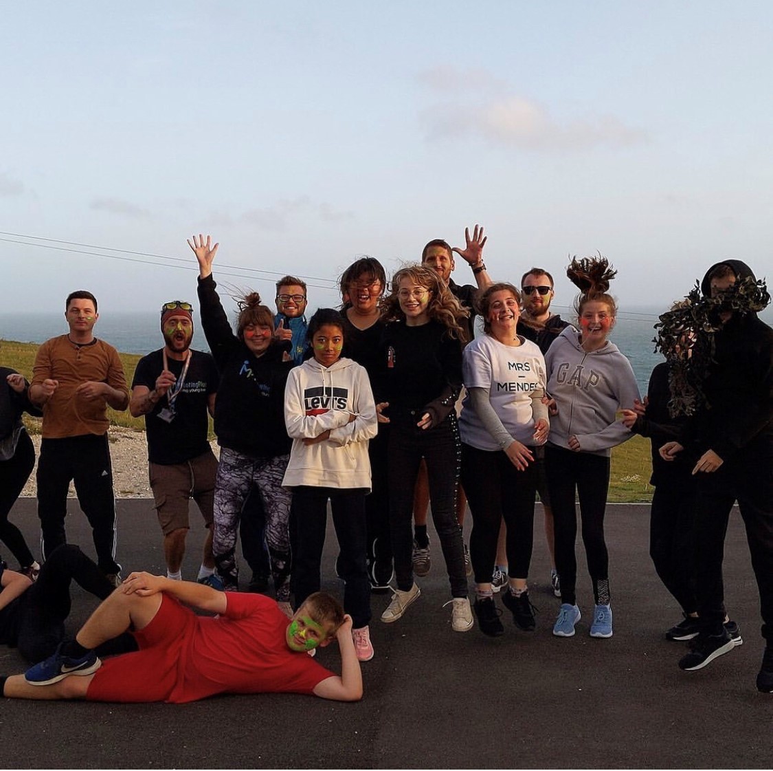 A group of young people and youth workers playing and posing together on a coastal path during a Mentoring Plus outing