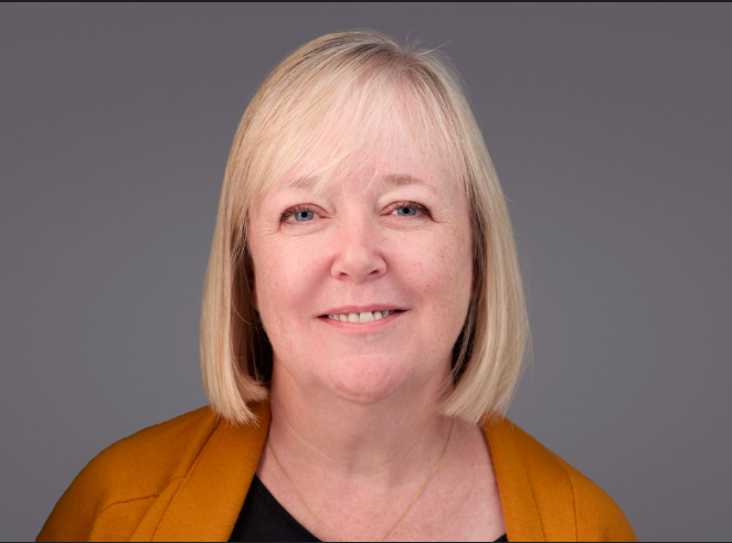 Ruth's headshot. She is smiling and wearing and orange cardigan. 