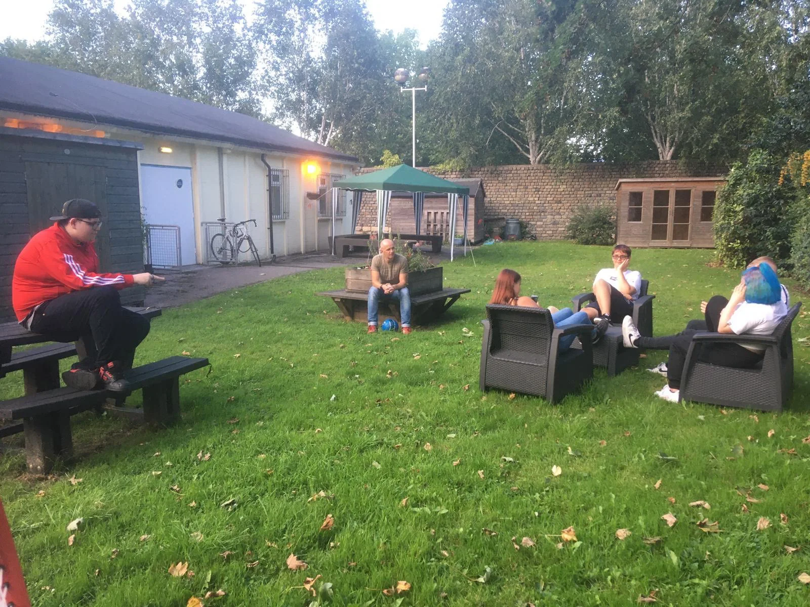 Four young people and a youth worker chatting outside on the grass at youth club on an autumn evening
