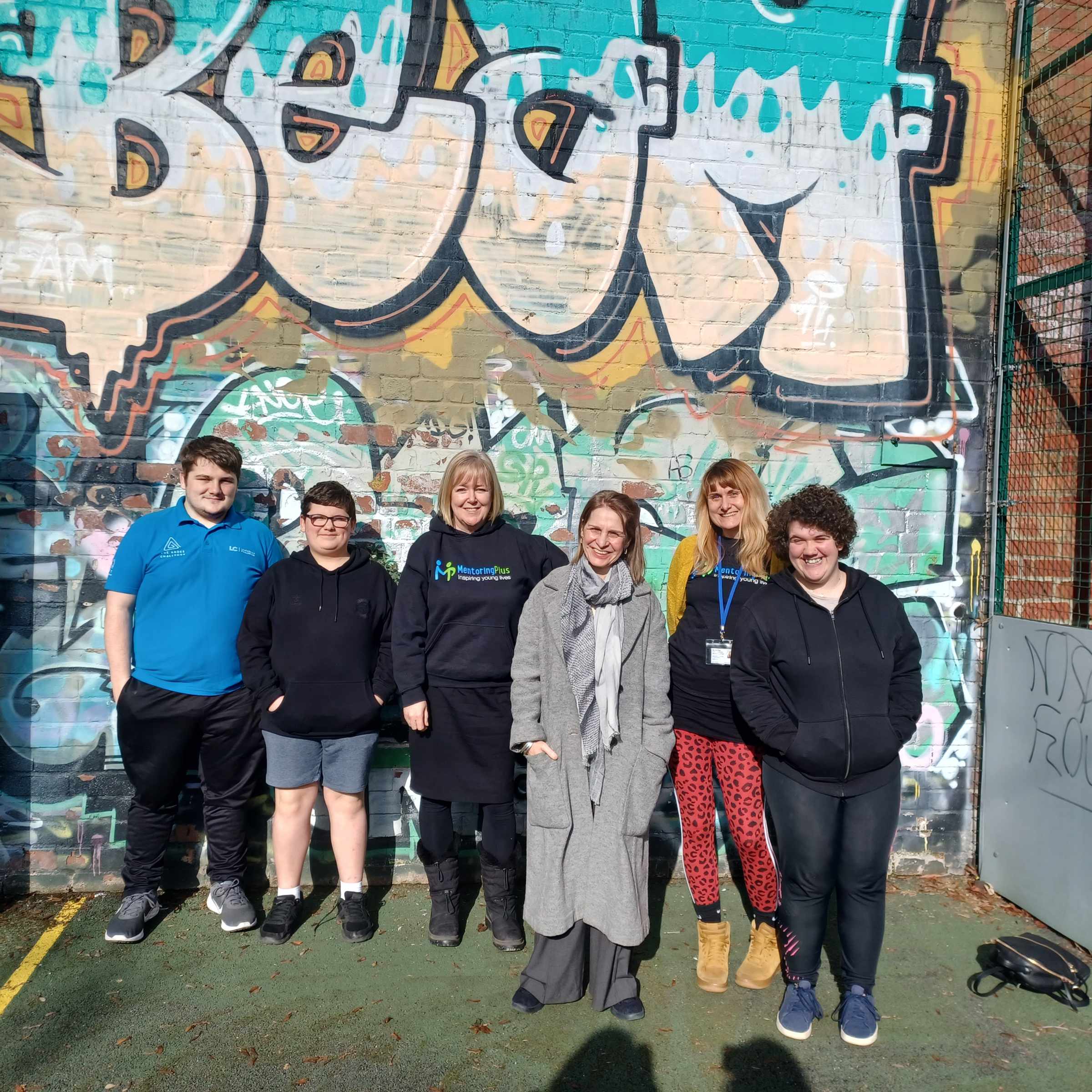 Mentoring Plus staff and a visitor standing together in front of a graffiti wall