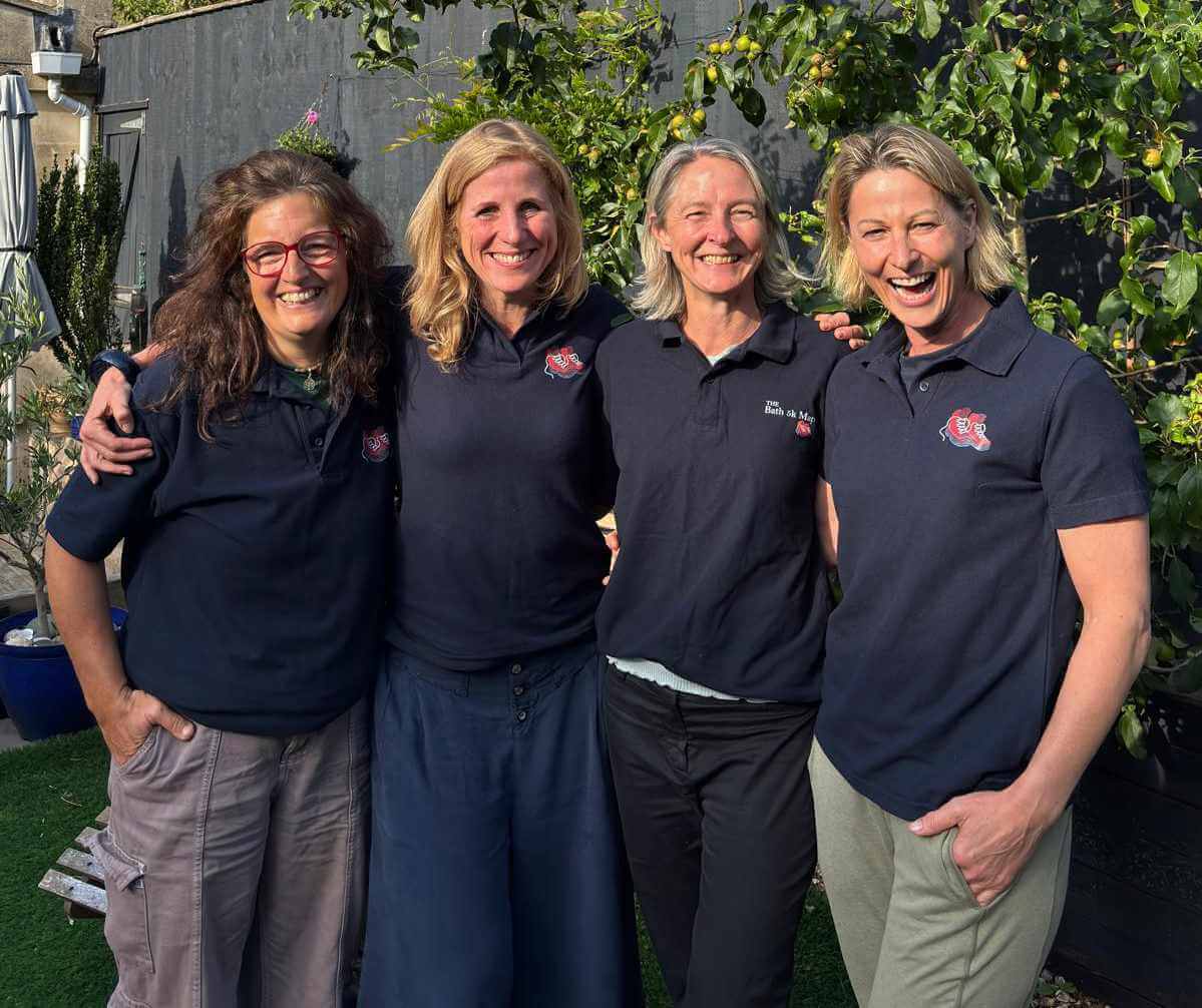 Four women in matching event shirts smiling together, taking part in a Mentoring Plus fundraising challenge