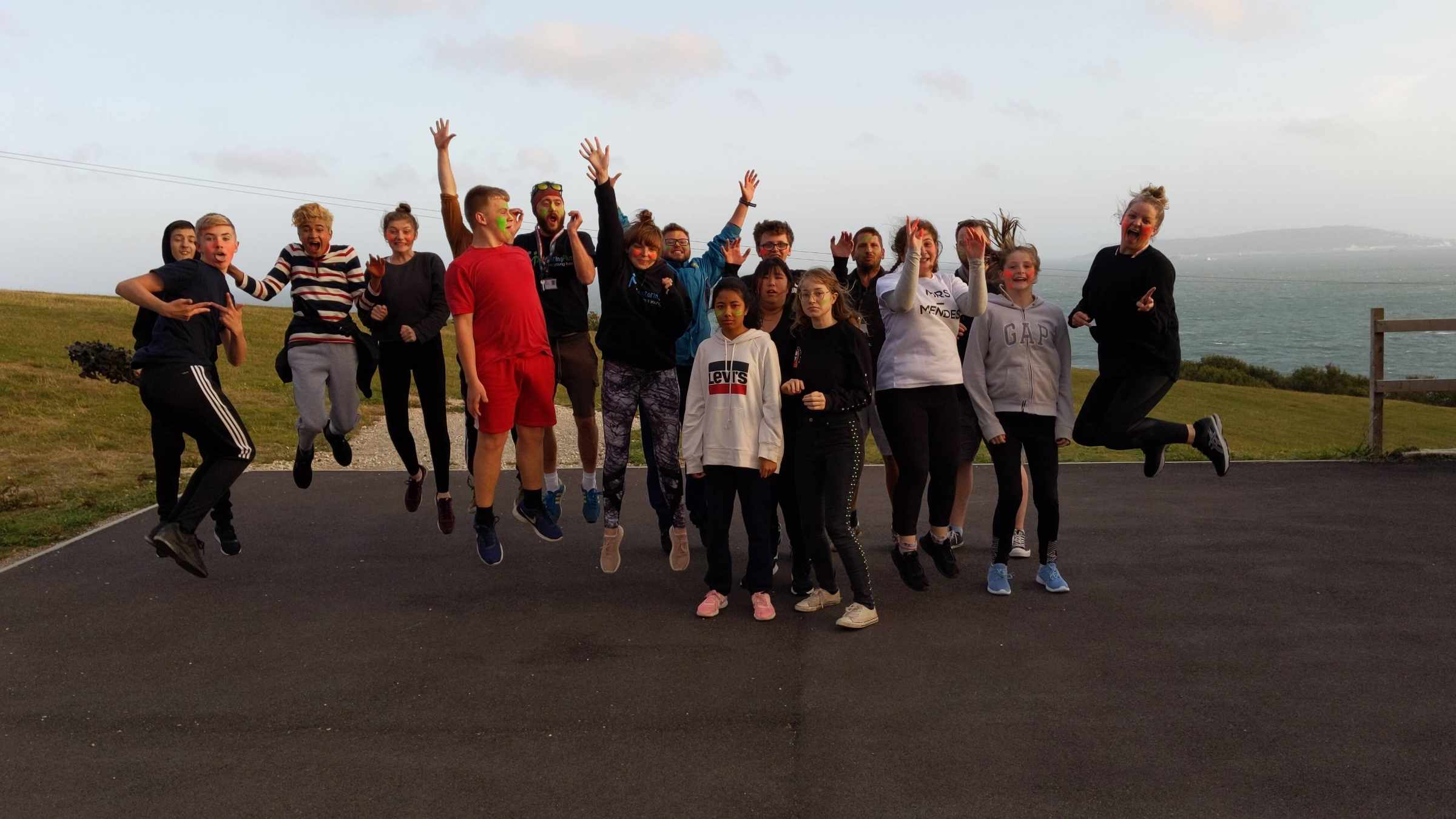 A large group of young people jumping together on a coastal path during a Mentoring Plus residential trip