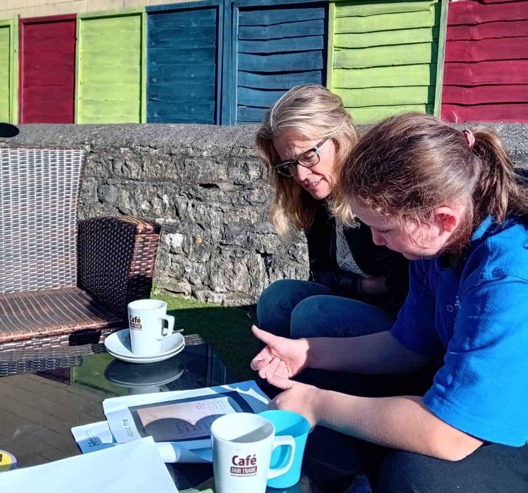 A mentor and young person sitting together outside a cafe, looking at a workbook during a mentoring session