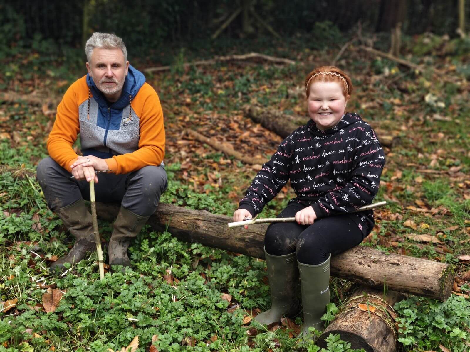 A mentor and young person sitting on a log during a bushcraft activity in the woods