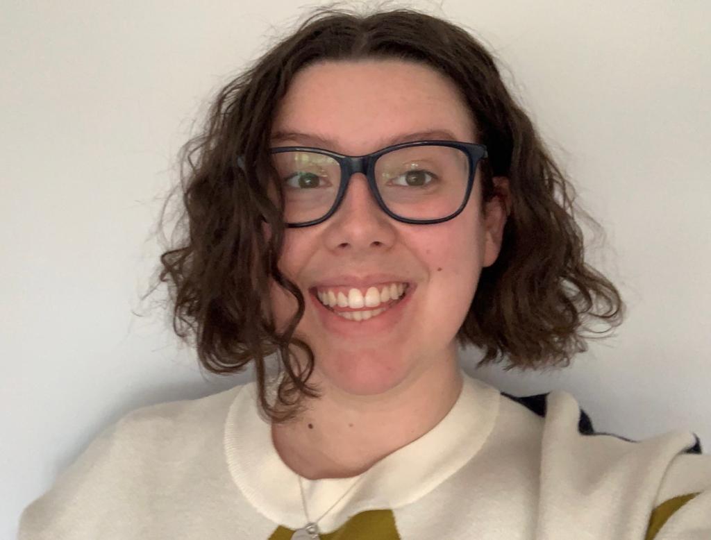 Photo of Harriet, she is smiling at the camera. She has glasses and brown hair, and is wearing a cream jumper