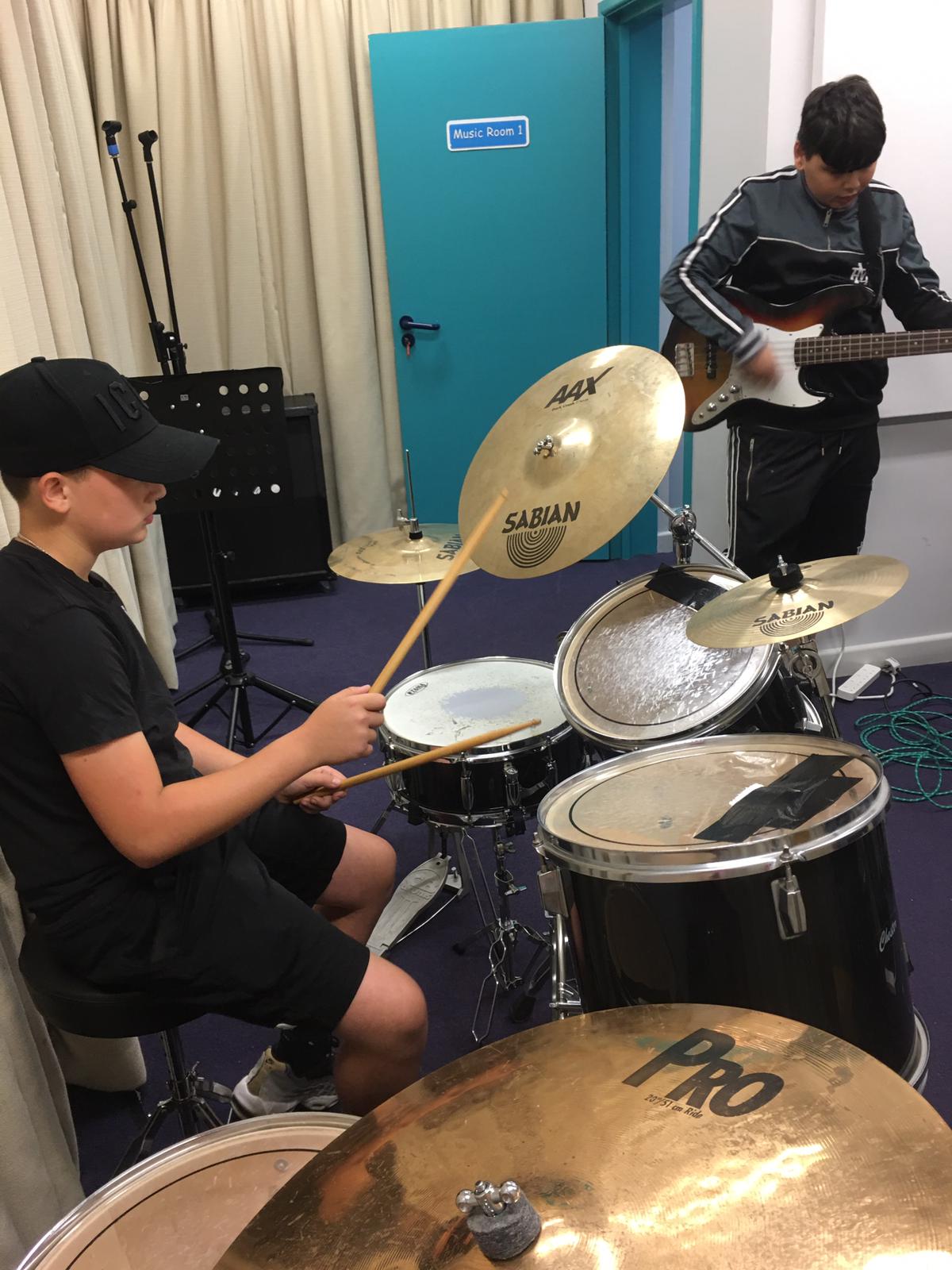 Young people playing drums and bass guitar together in a music room
