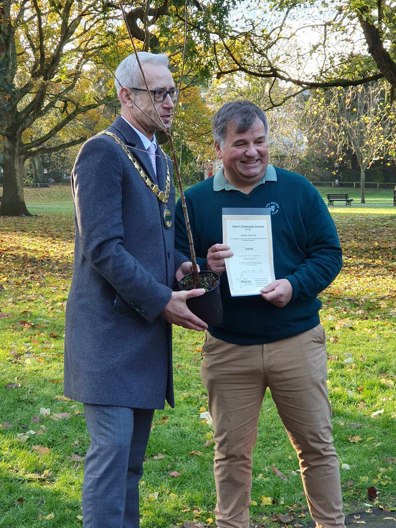 John Harvey receiving a community award certificate and a tree from the Mayor in a park