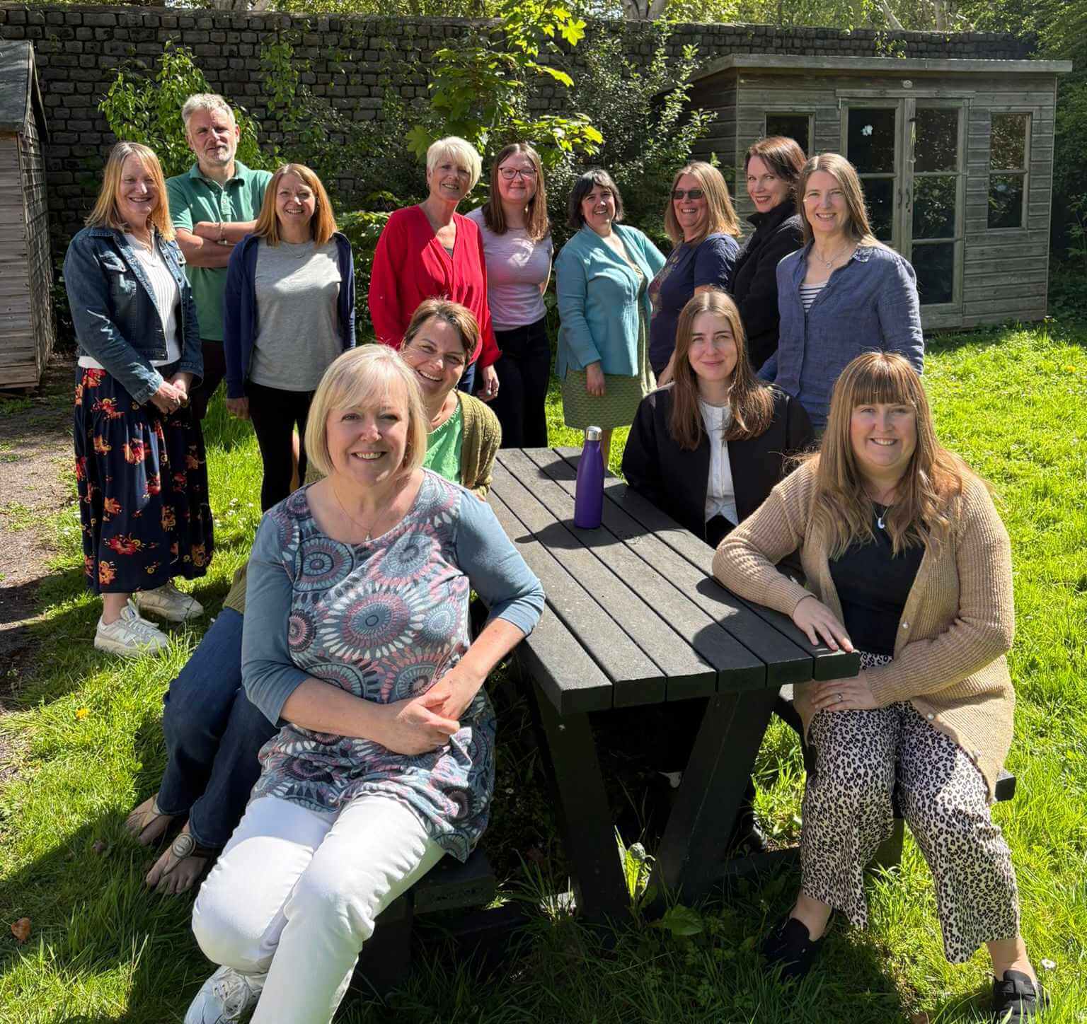 Mentoring Plus team grouped around a picnic bench smiling at the camera 