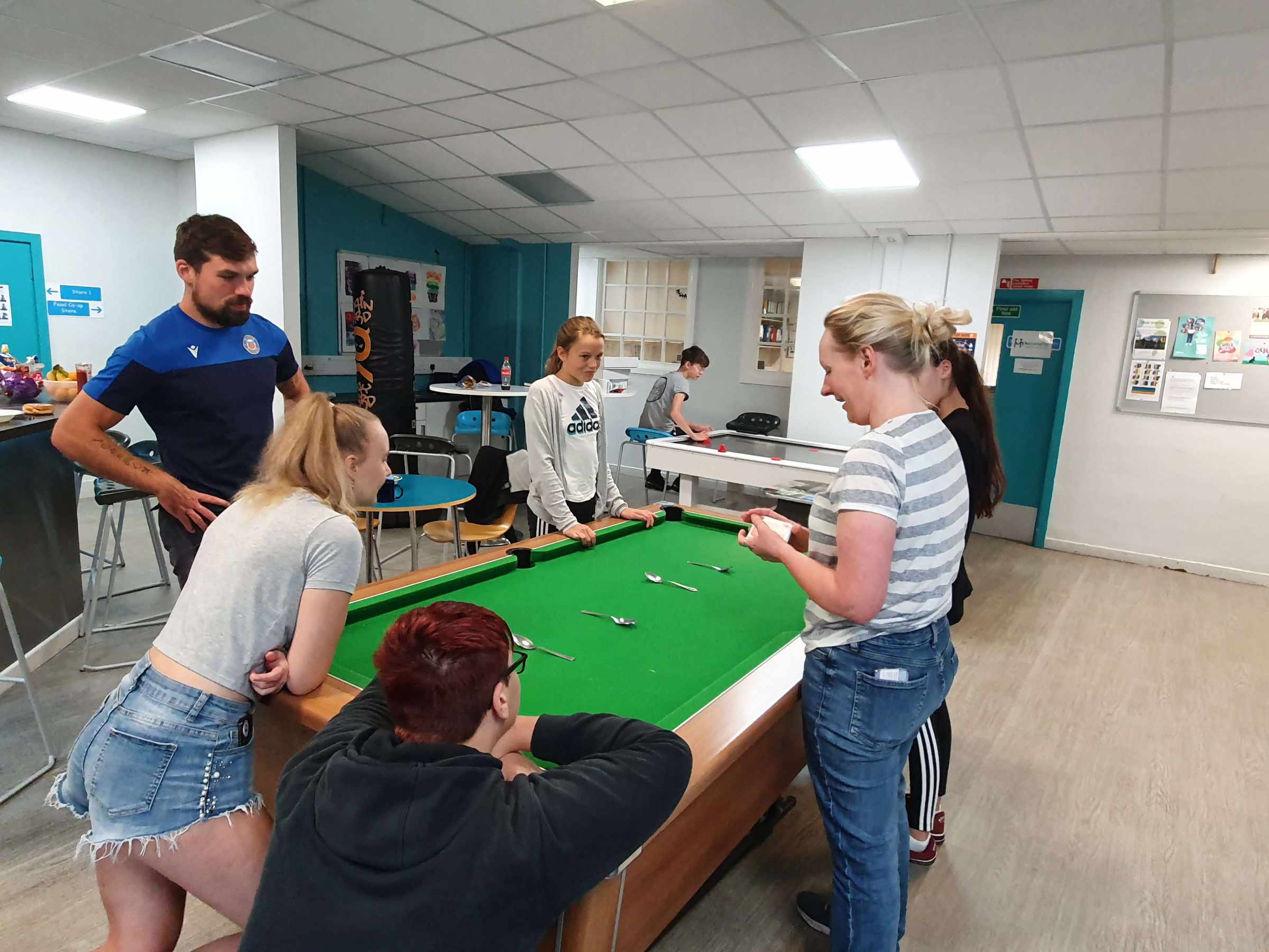 Young people and a youth worker playing a game around a pool table at a Mentoring Plus youth club