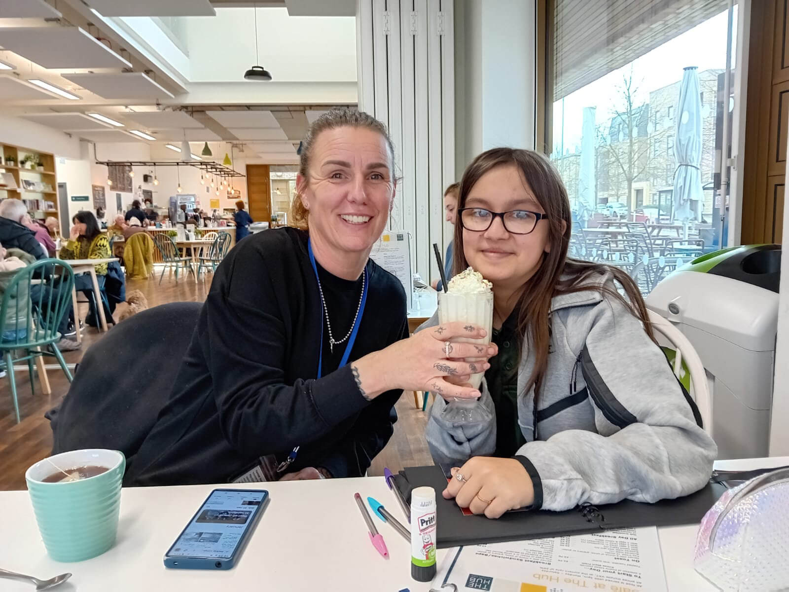 A mentor and young person sitting together in a cafe, sharing a milkshake and doing a craft activity