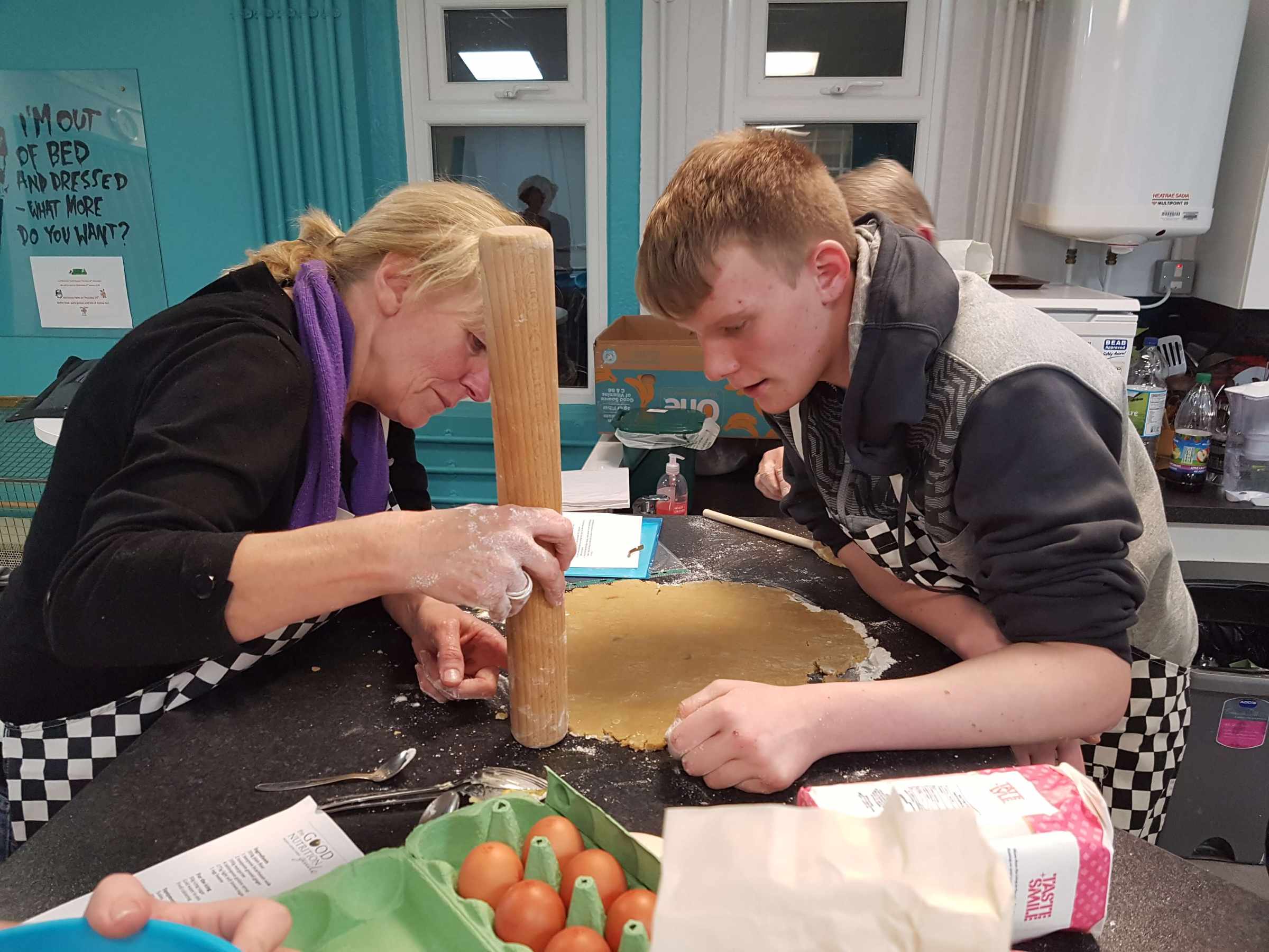 A mentor and young person rolling out pastry together in a kitchen
