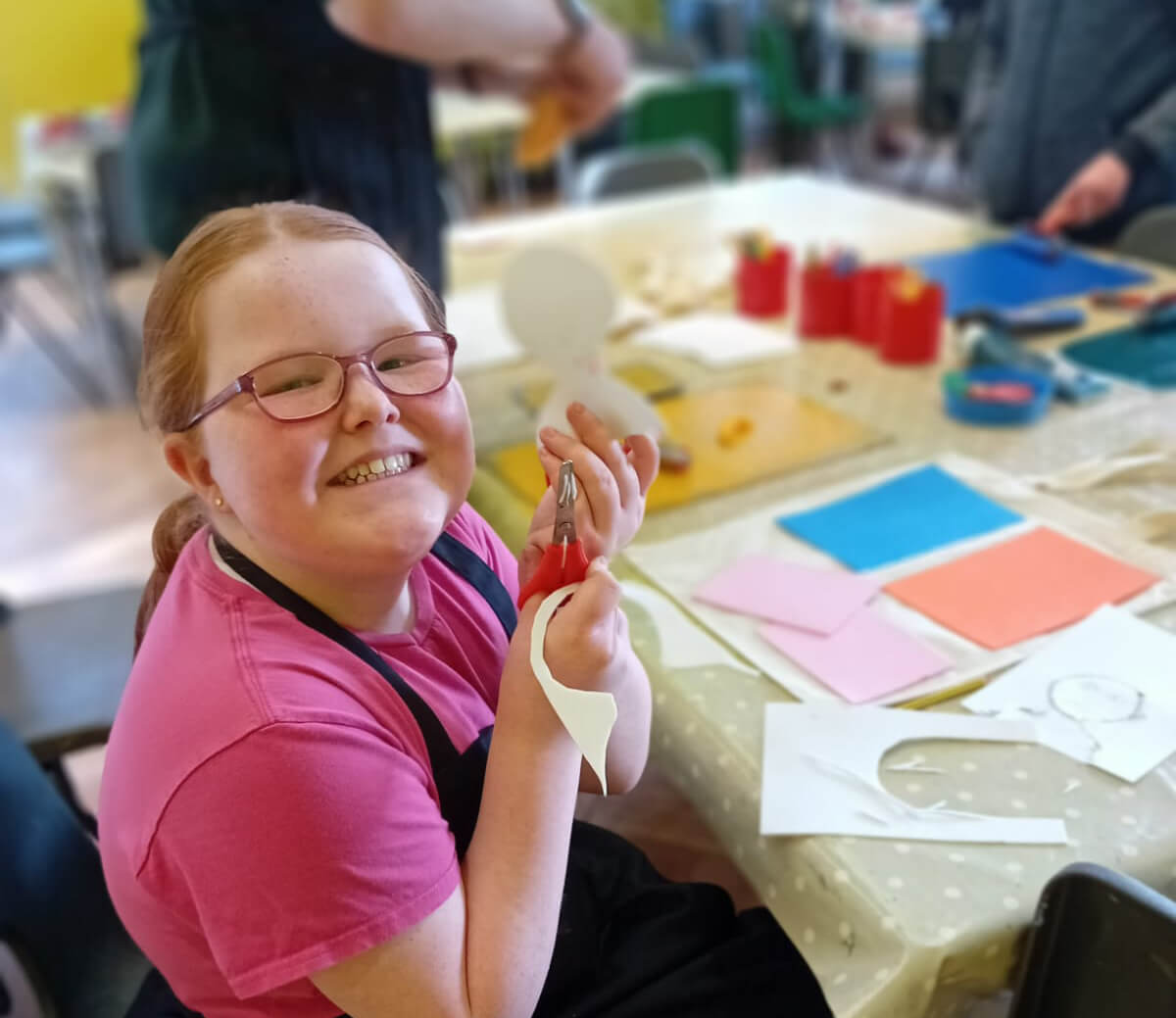 A girl smiling at the camera while doing crafts