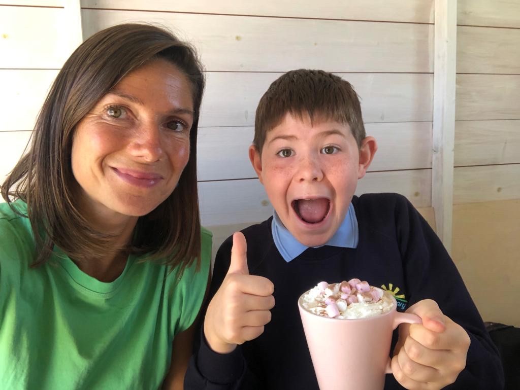 A mentor and young person smiling together, with the young person giving a thumbs up while holding a hot chocolate