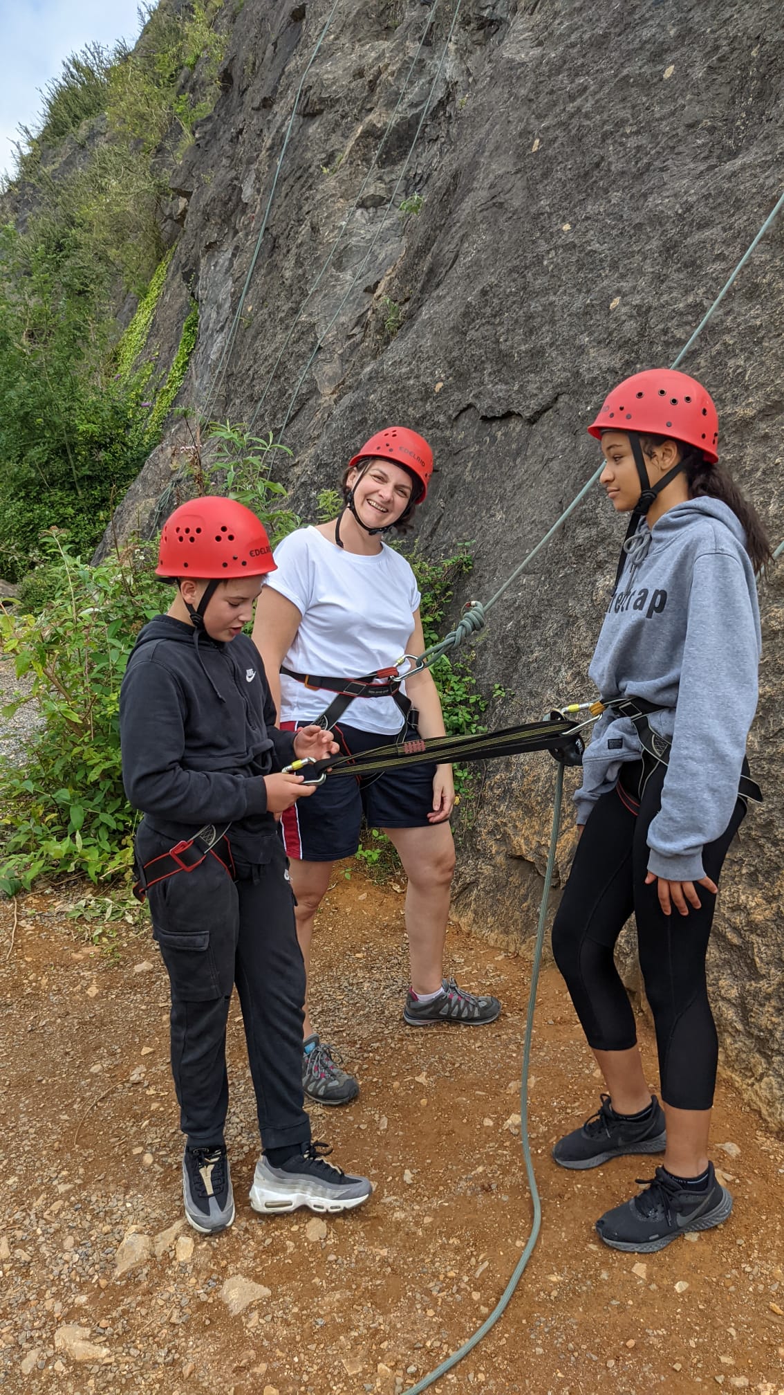Young people being shown how to use a climbing harness at the base of a rock face