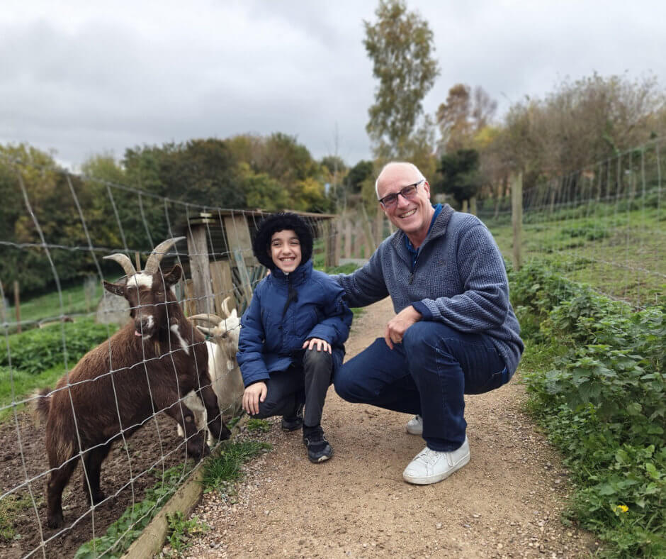 A Mentoring Plus volunteer with a young person crouched down next to the goats smiling at the camera