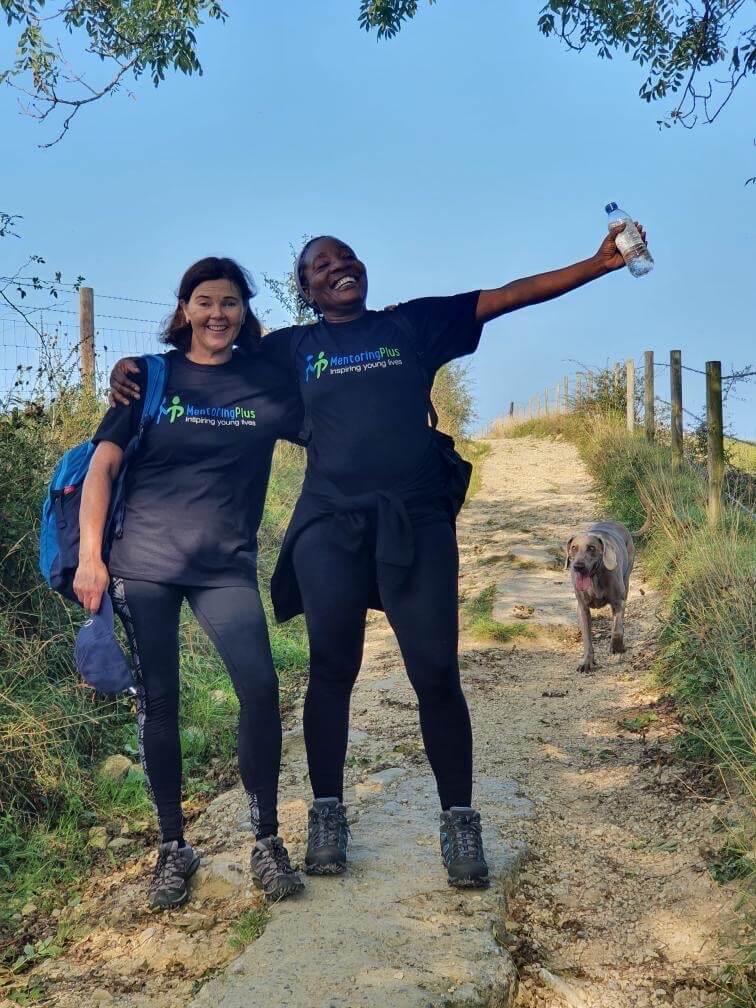 Two women wearing Mentoring Plus t shirts celebrating on a countryside trail during a fundraising walk